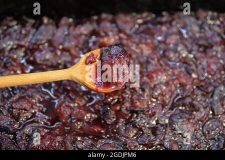 Prunes bouillies dans une cuillère en bois à la maison dans la cuisine. Le processus de fabrication de la confiture de prune Banque D'Images