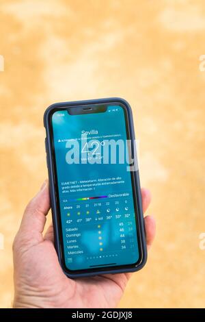 Séville, Espagne. 13 août 2021. Détail d'une main tenant un smartphone montrant une application météo. Le changement climatique provoque des températures exceptionnellement élevées Banque D'Images