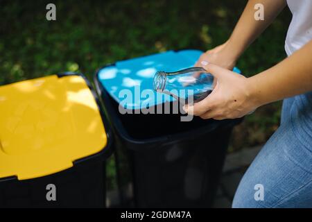 Gros plan portrait femme main throwig bouteille de verre vide dans le bac de recyclage. Différentes couleurs de bacs en plastique dans le parc Banque D'Images