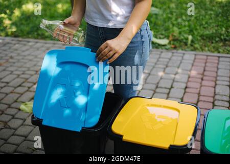 Gros plan portrait femme main throwig bouteille de verre vide dans le bac de recyclage. Différentes couleurs de bacs en plastique dans le parc Banque D'Images