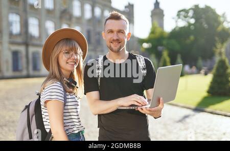 Étudier ensemble. Deux adorables étudiants, hommes et femmes, avec des sacs à dos utilisant un ordinateur portable sur le campus de l'université. Adorables étudiants réussis couple sourire en regardant l'appareil photo sourire. Photo de haute qualité Banque D'Images