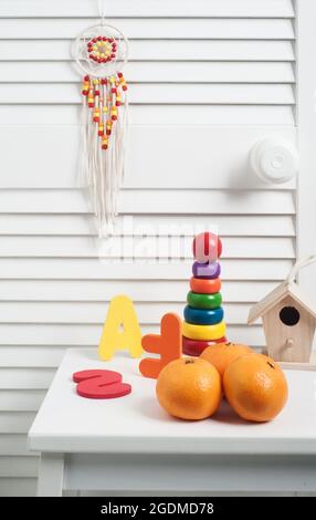 Cacher de rêve rustique avec des perles en bois rouge et jaune à l'intérieur avec des jouets, des lettres et des mandarines Banque D'Images