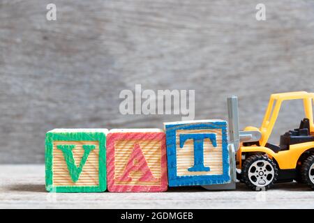 Chariot élévateur à jouets tenir la lettre T de couleur pour compléter le mot VAT (Abberviation de la taxe sur la valeur ajoutée) sur fond de bois Banque D'Images
