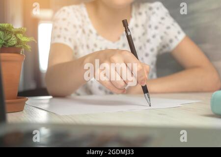 Fille étudiante tenant un crayon et écrivant sur un document papier dans le bureau. Table en bois avec ordinateur portable et espace de travail Banque D'Images