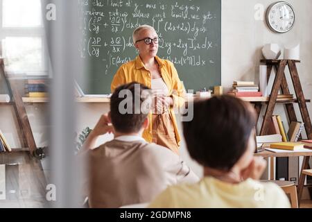 Professeur de mathématiques debout au tableau noir et expliquant le matériel aux élèves de la classe Banque D'Images
