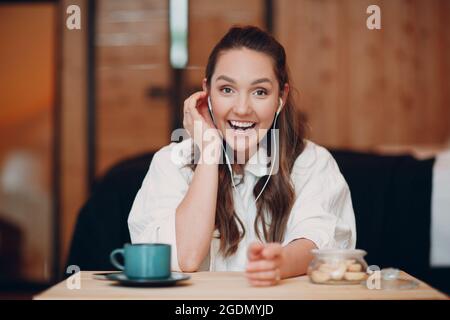 L'application d'écran affiche une jeune femme souriante s'asseoir à une table avec un ordinateur portable et parler lors d'un appel vidéo avec un ami ou un collègue, une fille heureuse avec une tasse de thé ou de café parlant en ligne sur la webcam conférence à l'intérieur. Banque D'Images