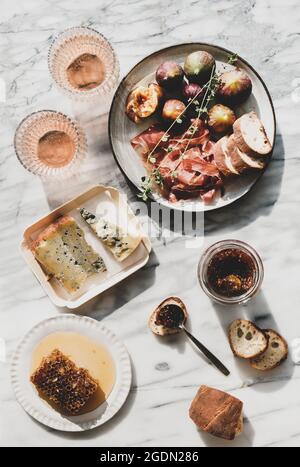 Plat de vin de rose dans des verres, nid d'abeille, fromage, confiture de figues dans un pot et une cuillère, morceaux de baguette et assiette avec des figues fraîches et de la viande prosciutto plus de g Banque D'Images