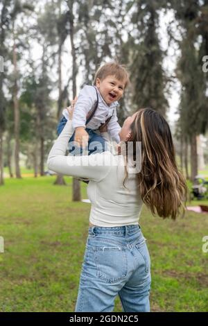 Photo verticale d'une mère qui élève son enfant en plein air en riant heureusement dans un parc urbain. Banque D'Images