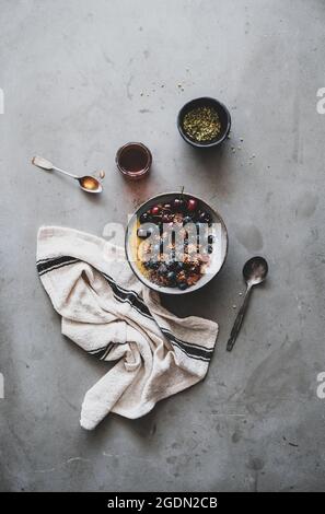 Petit-déjeuner végétalien sain. Télévision à jeter de l'avoine quinoa muesli yaourt coco bol à fruits, miel, noix, baies, graines de béton gris sur fond de table Banque D'Images