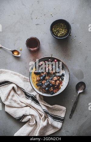 Petit-déjeuner végétalien sain. Télévision à jeter de l'avoine quinoa muesli yaourt coco bol à fruits, miel, noix, baies, graines de béton gris sur fond de table Banque D'Images