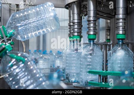 Les bouteilles en plastique de cinq litres sont remplies d'eau dans une machine de remplissage. Production automatisée d'eau potable. Production alimentaire Banque D'Images