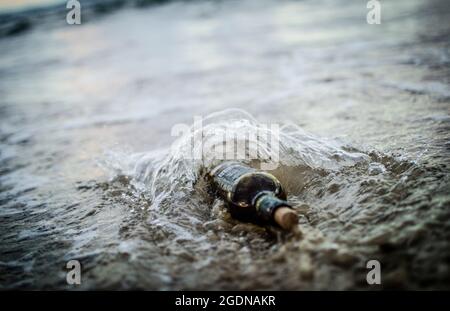 Message dans une bouteille - une bouteille à moitié enfouie dans le sable sur une plage Banque D'Images