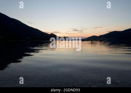 Lieu de méditation parfait. Avec de l'eau de lac translucide qui s'enlache sur des cailloux. Soleil orangé et reflets entre deux chaînes de montagnes alpines. Banque D'Images