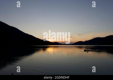 Un lieu de détente incroyable avec une traînée de soleil qui sépare la chaîne montagneuse d'arrière-plan de son reflet dans le lac alpin tranquille et le ponton Banque D'Images