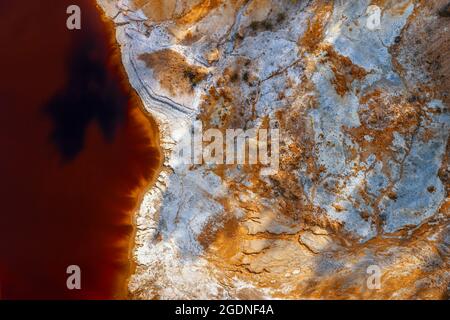 Rive couverte de produits chimiques et d'eau rouge du lac de la mine acide à la mine de cuivre opencast abandonnée, vue aérienne directement au-dessus Banque D'Images