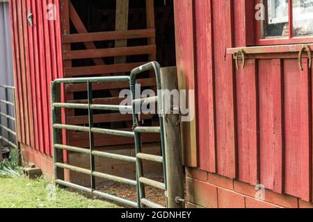 une ferme rustique rouge avec une porte fermée en métal vert rouille Banque D'Images