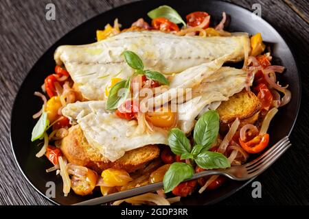 Gros plan de l'Acqua Pazza, poisson poché italien dans une sauce à base de tomate et de vin blanc avec fenouil, herbes et pain crostini croustillant sur une assiette noire, o Banque D'Images