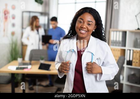 Médecine, santé et éducation. Portrait d'une femme afro professionnelle amicale médecin ou étudiante en médecine avec un stéthoscope, debout avec des collègues dans une clinique. Banque D'Images