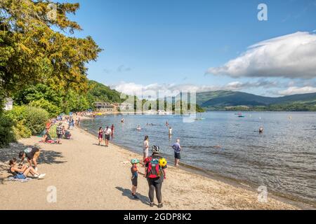 Personnes sur la plage à Luss à côté du Loch Lomond. Avec Lodge sur Loch Lomond et Ben Lomond en arrière-plan. Banque D'Images