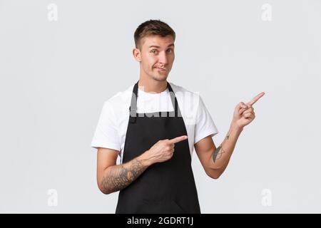 Concept des propriétaires de petites entreprises, du café et du personnel. Un beau barista en tablier noir qui donne aux clients des conseils, des smilk et des indications dans le coin supérieur droit Banque D'Images