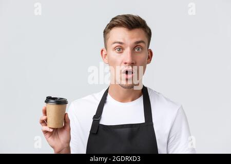 Café et restaurants, propriétaires de cafés et concept de vente au détail. Barista surpris et confus, serveur en tablier noir tenant une tasse en papier avec un plat à emporter Banque D'Images