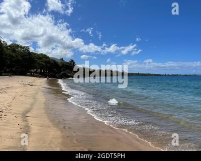 De grands nuages boursouflés pendent dans un ciel bleu immaculé tandis que les vagues de l'océan font le tour des rives dorées de la plage Ka'anapali à Lahaina, à Hawaï. Banque D'Images