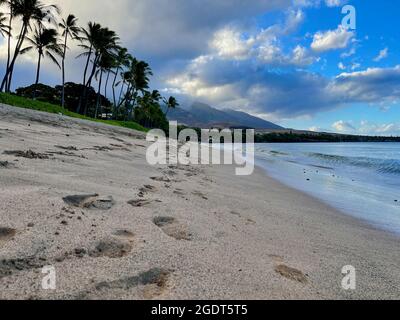 De grands nuages boursouflés pendent dans un ciel bleu immaculé tandis que les vagues de l'océan font le tour des rives dorées de la plage Ka'anapali à Lahaina, à Hawaï. Banque D'Images