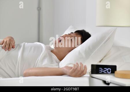 Jeune homme asiatique dormant et ronflant allongé dans le lit Banque D'Images