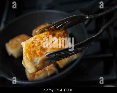 Rouleau de chou frit farci recouvert d'une croûte délicate dans des pinces de cuisine en métal. Processus de cuisson des petits pains de chou faits maison. Gros plan de la nourriture. BL non focalisé Banque D'Images