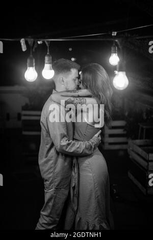 Portrait d'un couple aimant debout dans la barre sombre avec des lanternes, câliner et regarder dans les yeux. Image en noir et blanc. Photo de haute qualité Banque D'Images