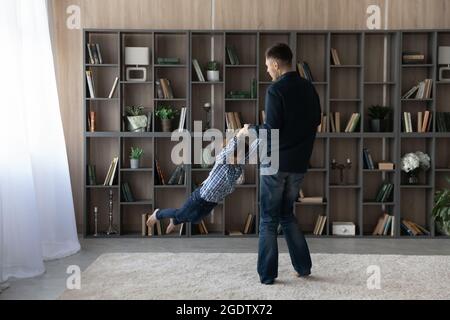 Un jeune papa fait tourner son fils pour s'amuser ensemble dans le salon Banque D'Images