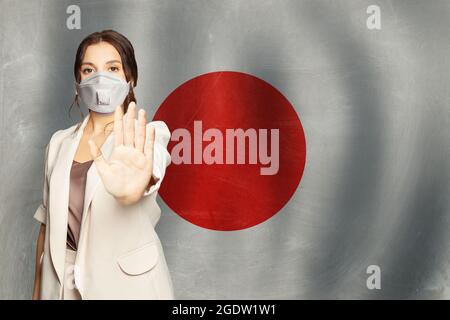 Prévention du coronavirus COVID-19 au Japon concept. Femme dans un masque de protection anti-virus montrant un geste d'arrêt sur fond de drapeau japonais Banque D'Images