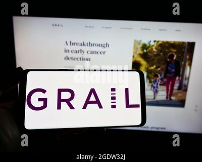 Personne tenant un téléphone cellulaire avec le logo de la société américaine de biotechnologie GRAAL Inc. À l'écran devant la page Web. Mise au point sur l'affichage du téléphone. Banque D'Images