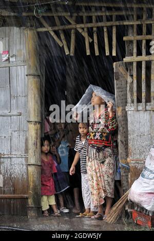 Les jeunes de la tribu indigène Blaan se réfugient à l'abri de la pluie tropicale. Village de Maligo Blaan, Brgy. Maligo. Mindanao Island, Philippines Banque D'Images