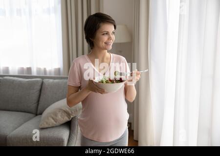 Bonne jeune femme enceinte tenant un bol avec de la salade de légumes frais Banque D'Images