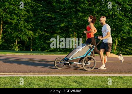 couple de course avec enfant dans la poussette de jogging dans le parc public au lever du soleil. Course matinale pour toute une famille Banque D'Images