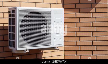 Gros plan d'une unité de climatisation moderne sur le fond d'un mur de briques de la façade d'une maison à l'extérieur. Air conditionné au mur wi Banque D'Images