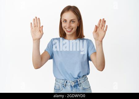 L'image d'une jeune femme heureuse souriant, levant les mains dans la reddition, n'a rien, montrant les paumes vides, debout dans un t-shirt sur fond blanc Banque D'Images