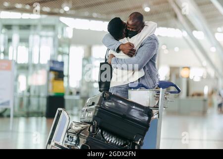 Couple africain se donnant un chaud câlin à l'arrivée de l'aéroport. Jeune homme et jeune femme se rencontrent à l'aéroport pendant une pandémie. Banque D'Images