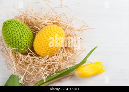 Œufs de pâques crochetés jaunes verts avec tulipe sur fond blanc Banque D'Images