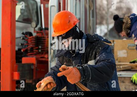 Portrait d'un ajusteur slinger dans un casque et gilet orange sur le déchargement des plaques de glace Banque D'Images