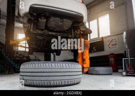 Centre de service de voiture. Bas derrière le véhicule pov soulevé sur le technicien de levage travailleur effectuer des diagnostics et l'inspection au poste de maintenance . Automobile Banque D'Images