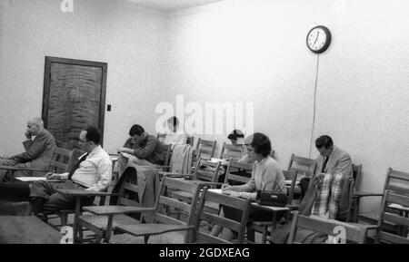 Années 1960, histoire, études complémentaires, lors d'un cours du soir, un petit groupe d'étudiants matures assis dans une classe faisant des notes écrites sur les chaises-bureaux traditionnels en bois de l'époque, Etats-Unis. Les bureaux d'école ont une histoire intéressante et la vieille école, ensemble chaise-bureau non réglable vu ici, était juste l'un des nombreux styles de bureau qui ont été introduits dans la salle de classe au fil des ans. Banque D'Images