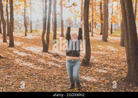 Un enfant heureux qui jette les feuilles tombées en jouant dans le parc d'automne. Banque D'Images