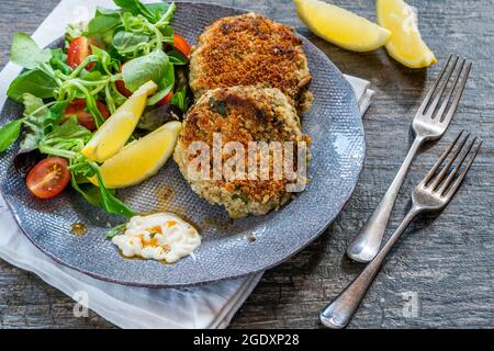 Gâteaux de poisson sardine avec salade de feuilles vertes, mayonnaise à l'ail et quartiers de citron Banque D'Images