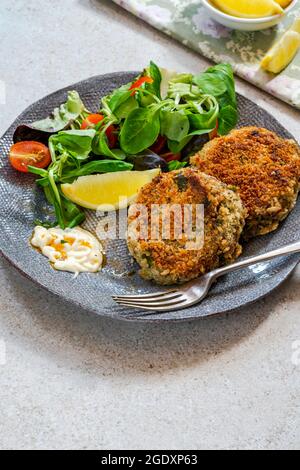 Gâteaux de poisson sardine avec salade de feuilles vertes, mayonnaise à l'ail et quartiers de citron Banque D'Images