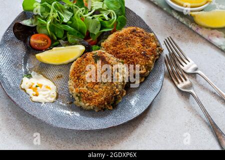 Gâteaux de poisson sardine avec salade de feuilles vertes, mayonnaise à l'ail et quartiers de citron Banque D'Images