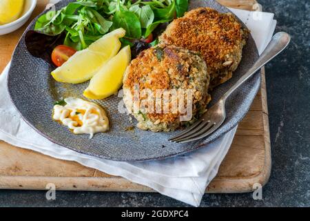 Gâteaux de poisson sardine avec salade de feuilles vertes, mayonnaise à l'ail et quartiers de citron Banque D'Images