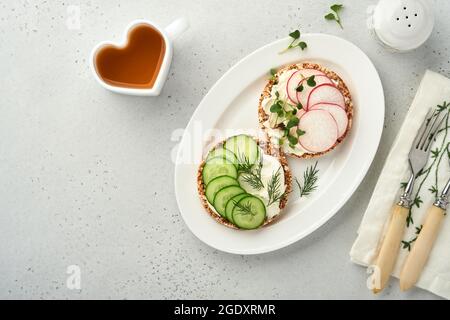 Deux gâteaux croustillants de sarrasin sans gluten avec fromage à la crème, radis rouge, concombre et microgreen pour un petit déjeuner sain sur fond de pierre grise. VI Banque D'Images