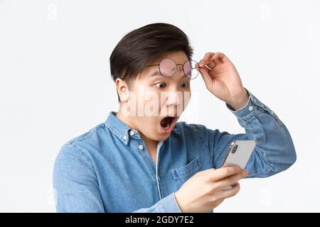 Gros plan sur les lunettes de décollage choquées d'un homme asiatique, qui se déchagent en regardant l'écran du téléphone mobile, en lisant des nouvelles choquantes, réagissent à l'annonce Banque D'Images